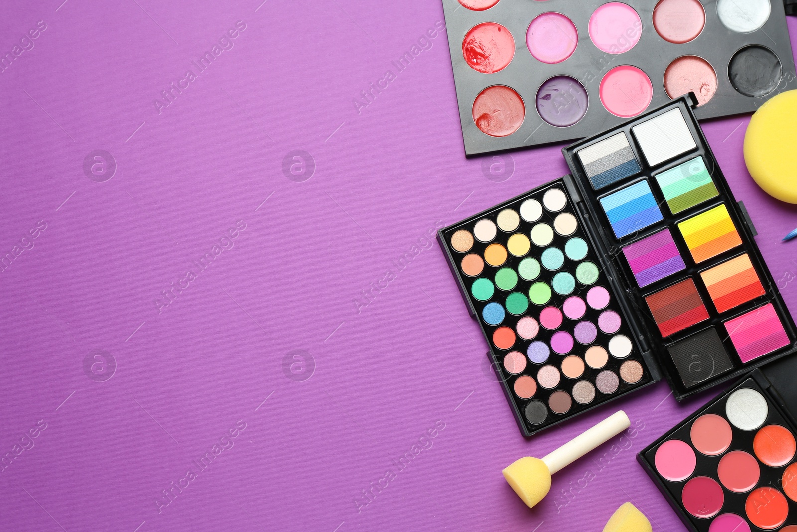 Photo of Face paints, tools and makeup products on purple background, flat lay. Space for text