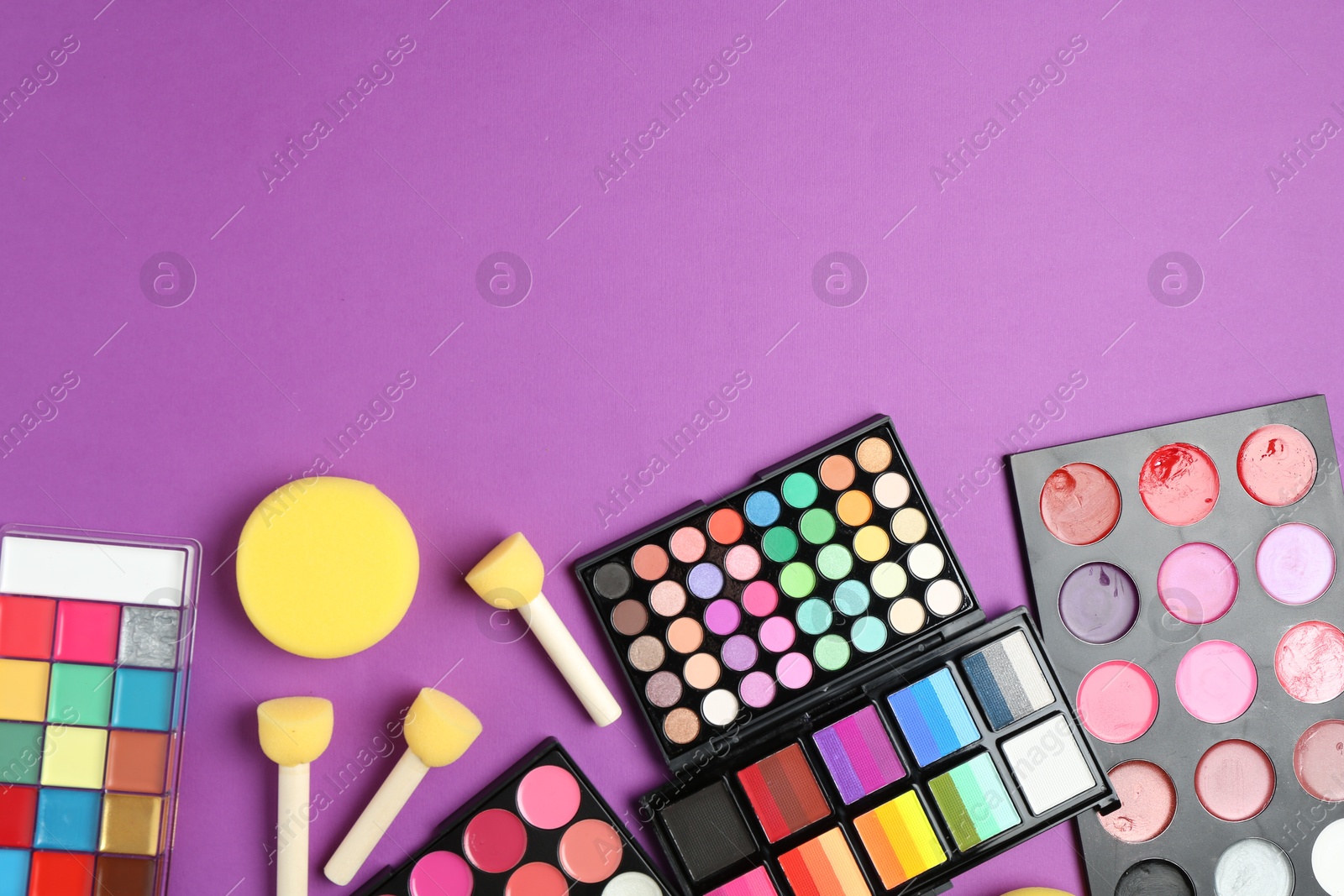 Photo of Face paints, tools and makeup products on purple background, flat lay. Space for text