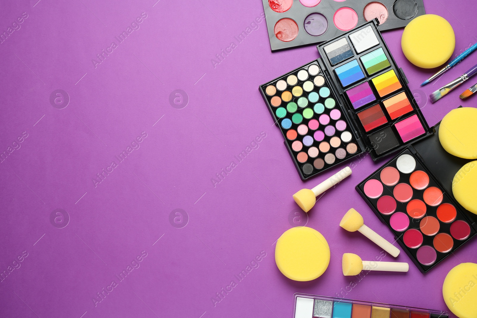 Photo of Face paints, tools and makeup products on purple background, flat lay. Space for text