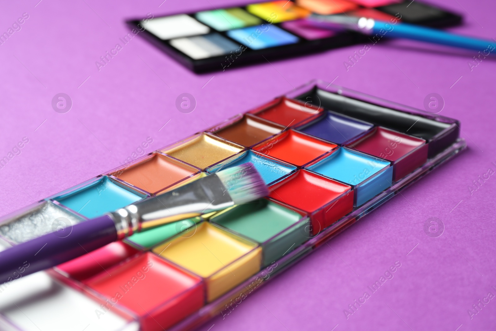 Photo of Face paints and tools on purple background, closeup