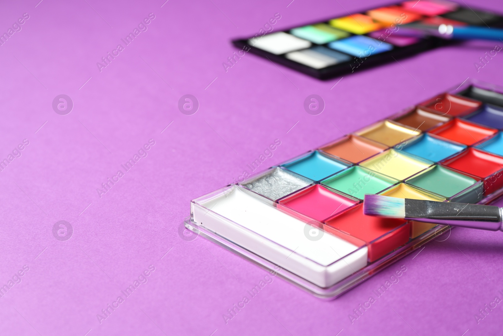 Photo of Face paints and tools on purple background, closeup. Space for text