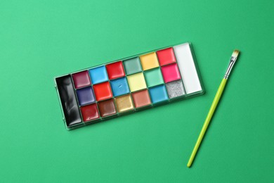 Photo of Face paints and brush on green background, top view