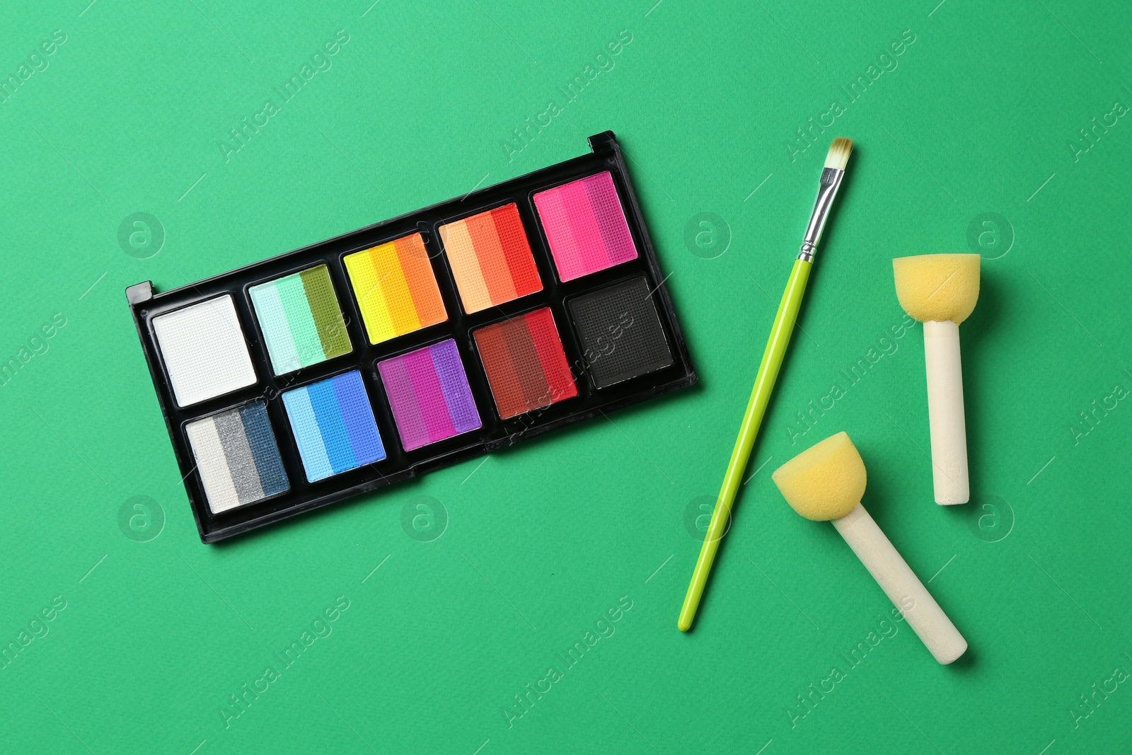 Photo of Face paints and tools on green background, flat lay