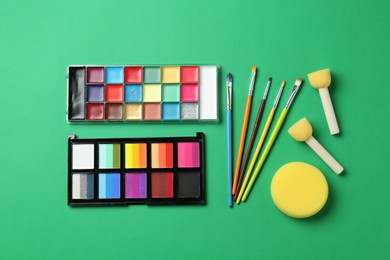 Photo of Face paints and tools on green background, flat lay