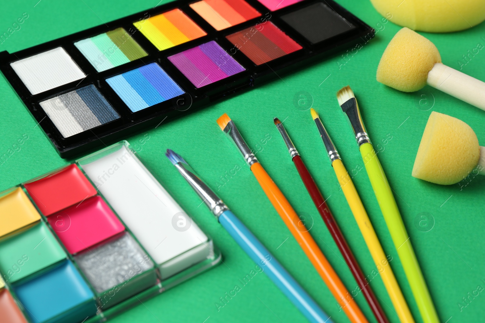 Photo of Face paints and tools on green background, closeup