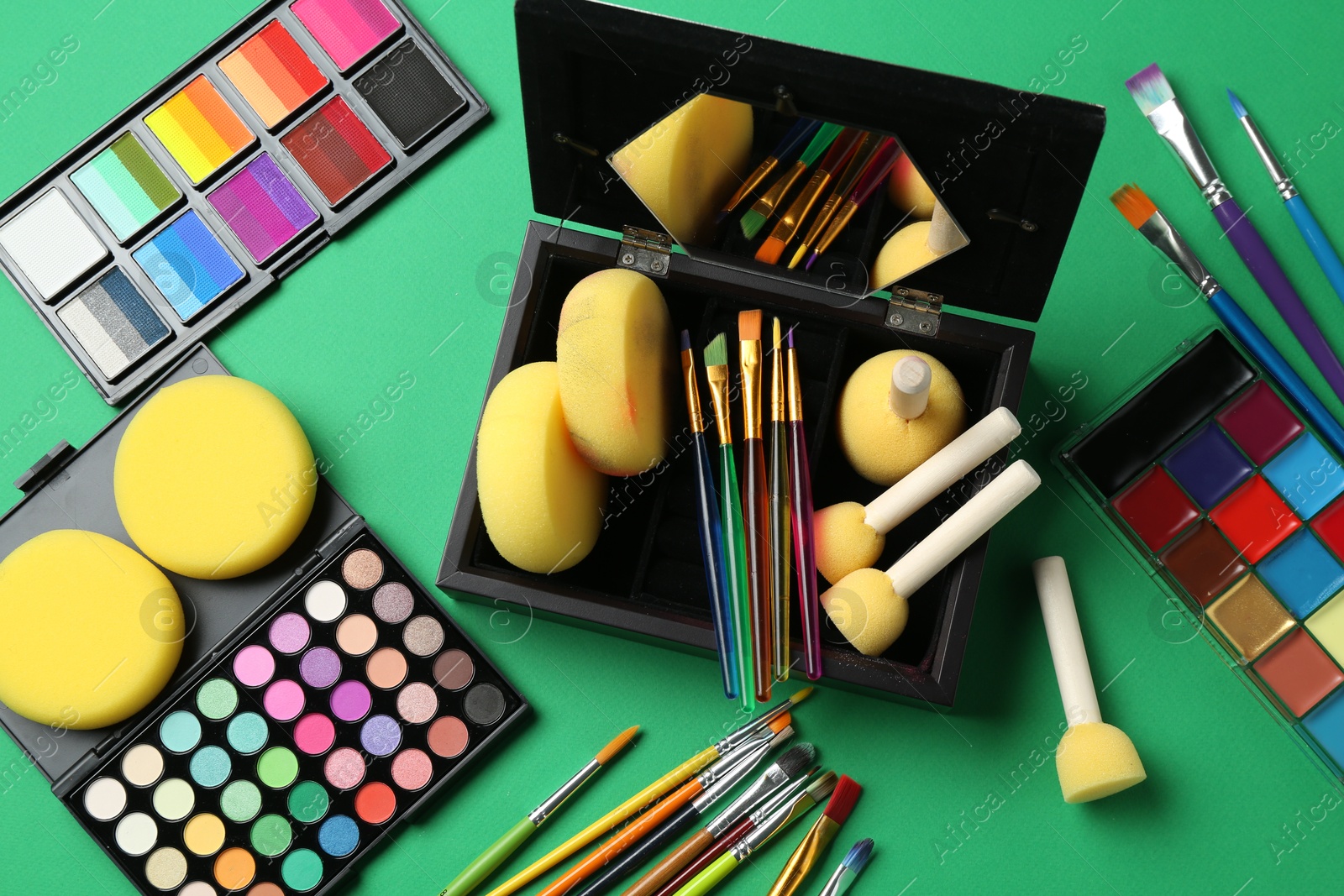 Photo of Face paints, tools and makeup products on green background, flat lay