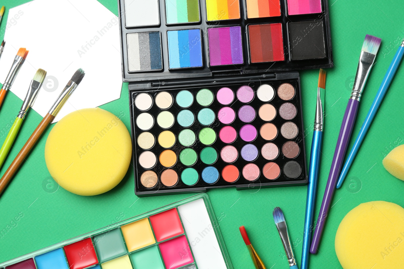 Photo of Face paints, tools and makeup products on green background, flat lay