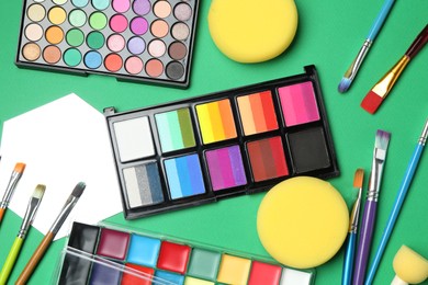 Photo of Face paints, tools and makeup products on green background, flat lay