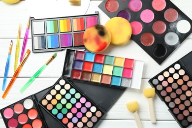 Photo of Face paints, tools and makeup products on white wooden background, flat lay