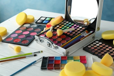 Photo of Face paints, tools and makeup products on white wooden table, closeup