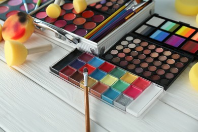 Photo of Face paints, tools and makeup products on white wooden background, closeup