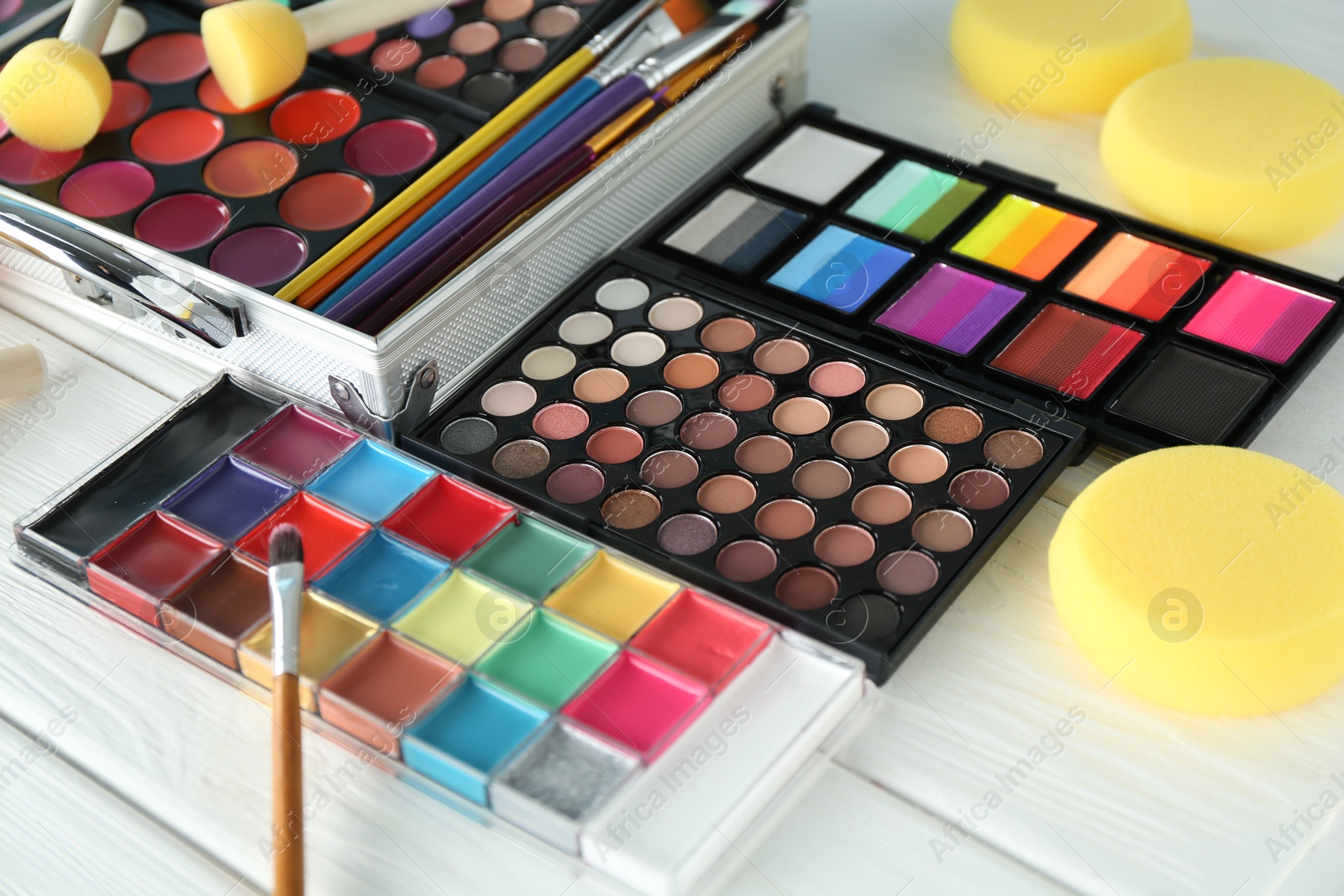 Photo of Face paints, tools and makeup products on white wooden background, closeup