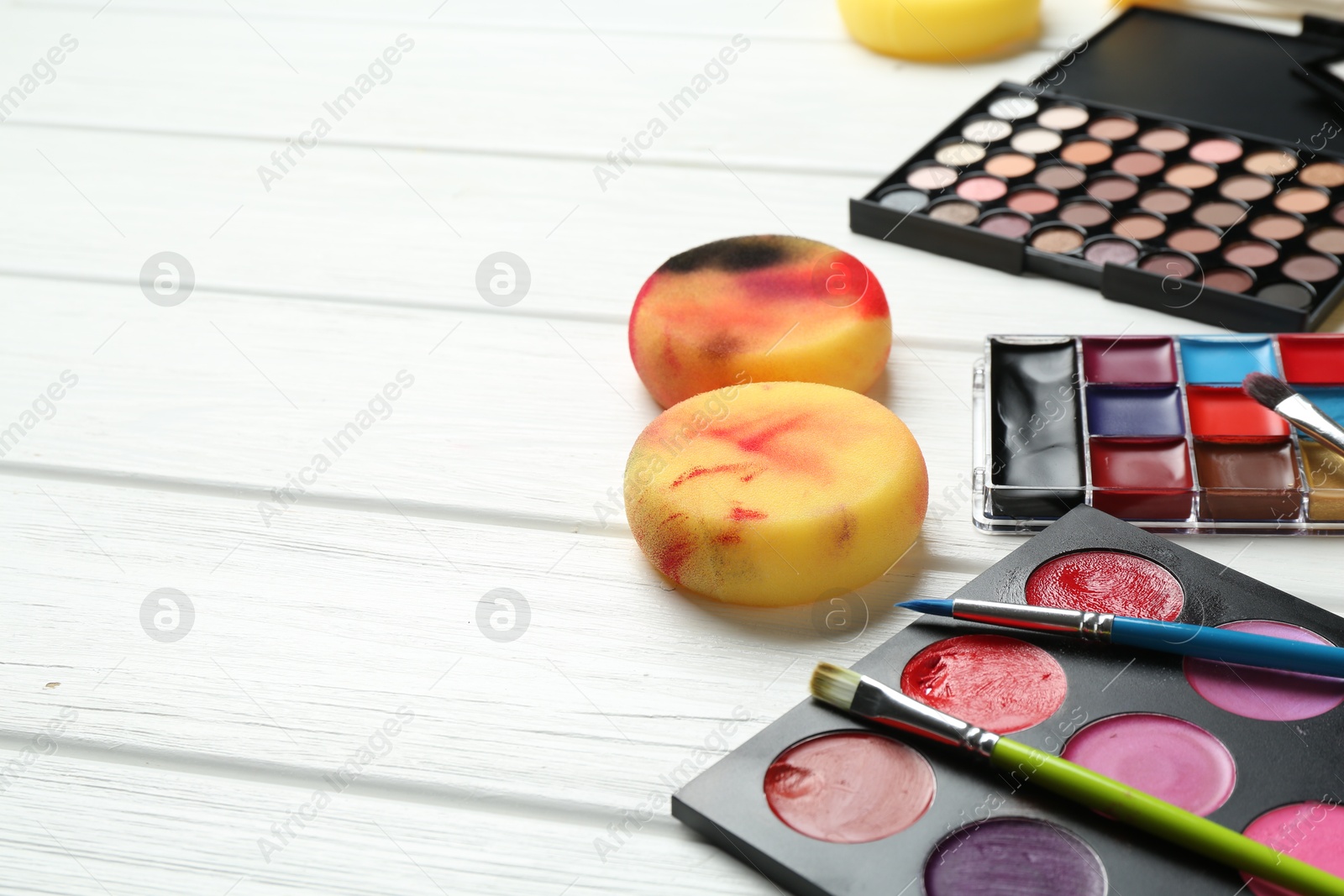 Photo of Face paints, tools and makeup products on white wooden background, closeup. Space for text