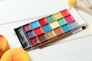 Photo of Face paints and tools on white wooden background, closeup