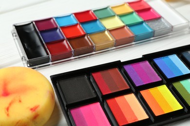 Photo of Face paints and sponge on white wooden table, closeup