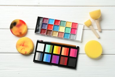 Photo of Face paints and tools on white wooden background, flat lay