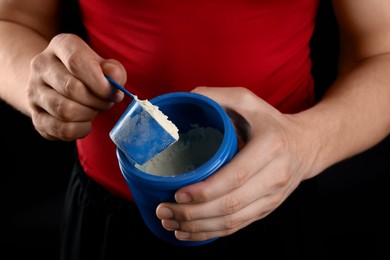 Photo of Sportsman taking protein with scoop on dark background, closeup