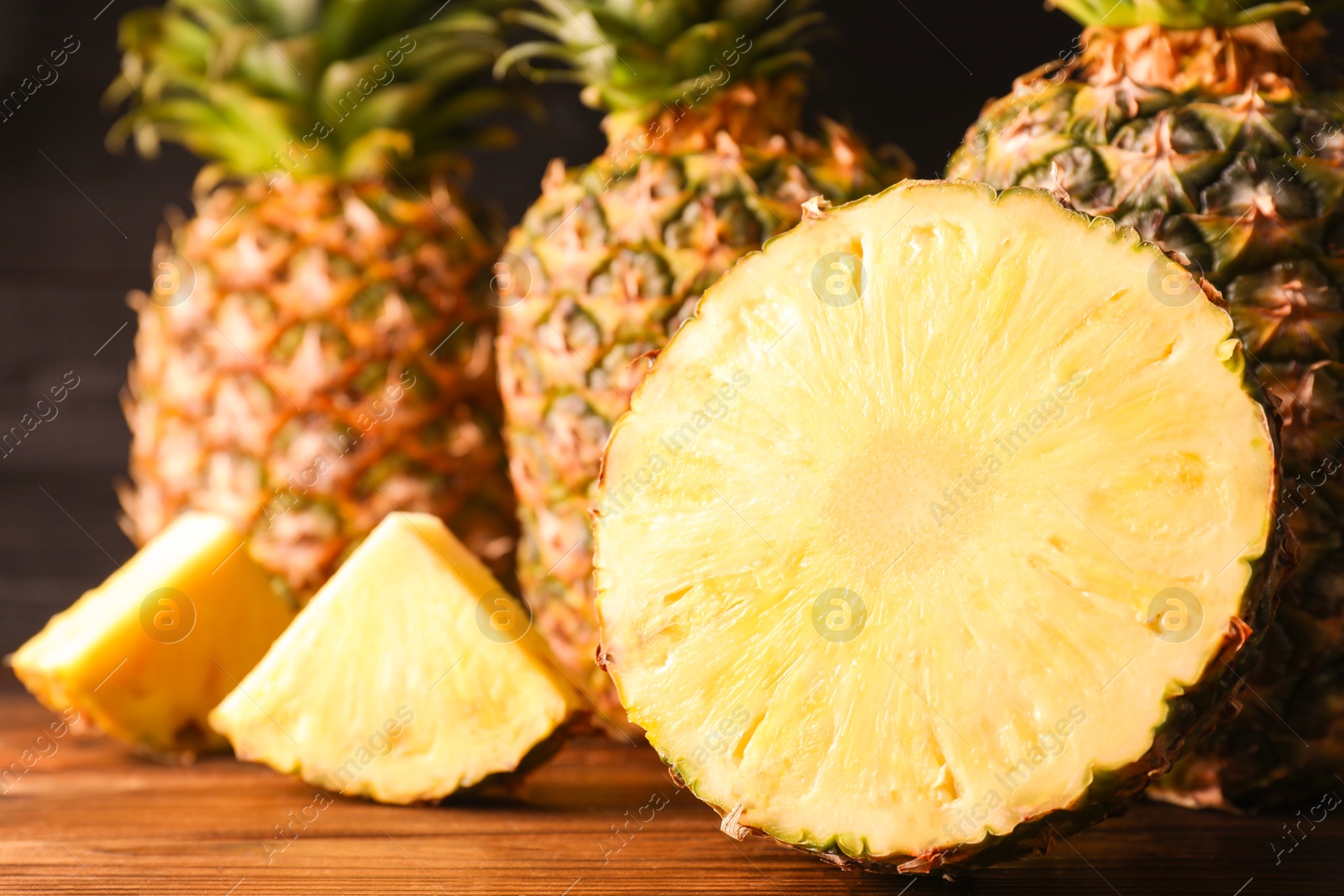 Photo of Whole and cut ripe pineapples on wooden table, closeup