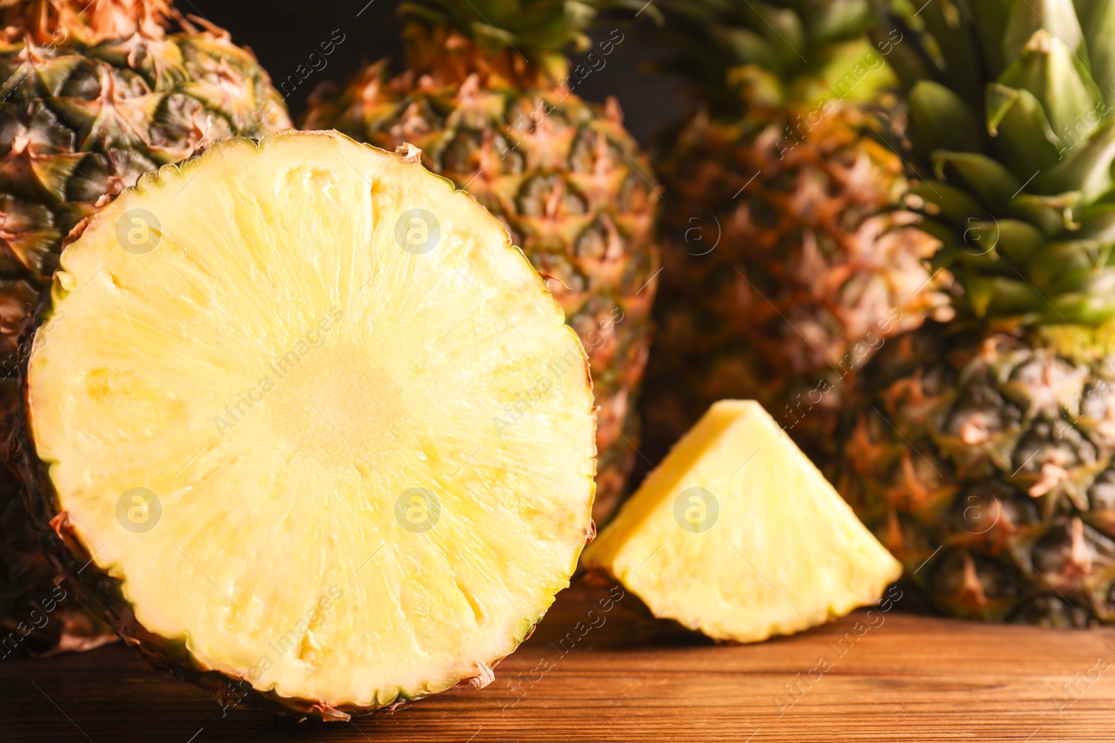 Photo of Whole and cut ripe pineapples on wooden table, closeup