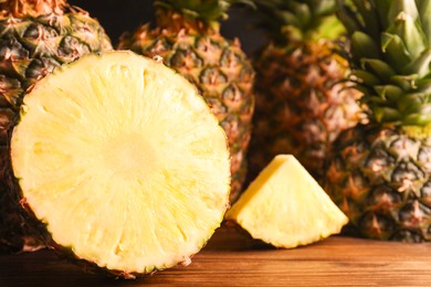 Photo of Whole and cut ripe pineapples on wooden table, closeup