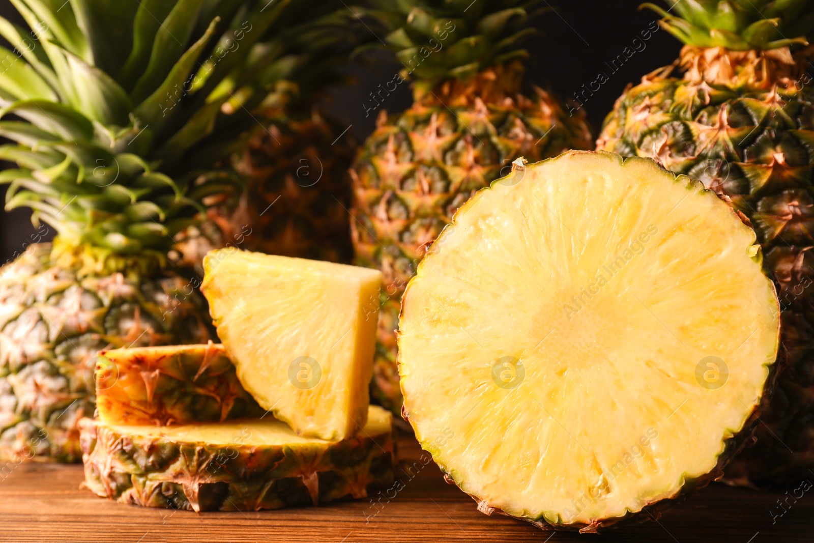 Photo of Whole and cut ripe pineapples on wooden table, closeup