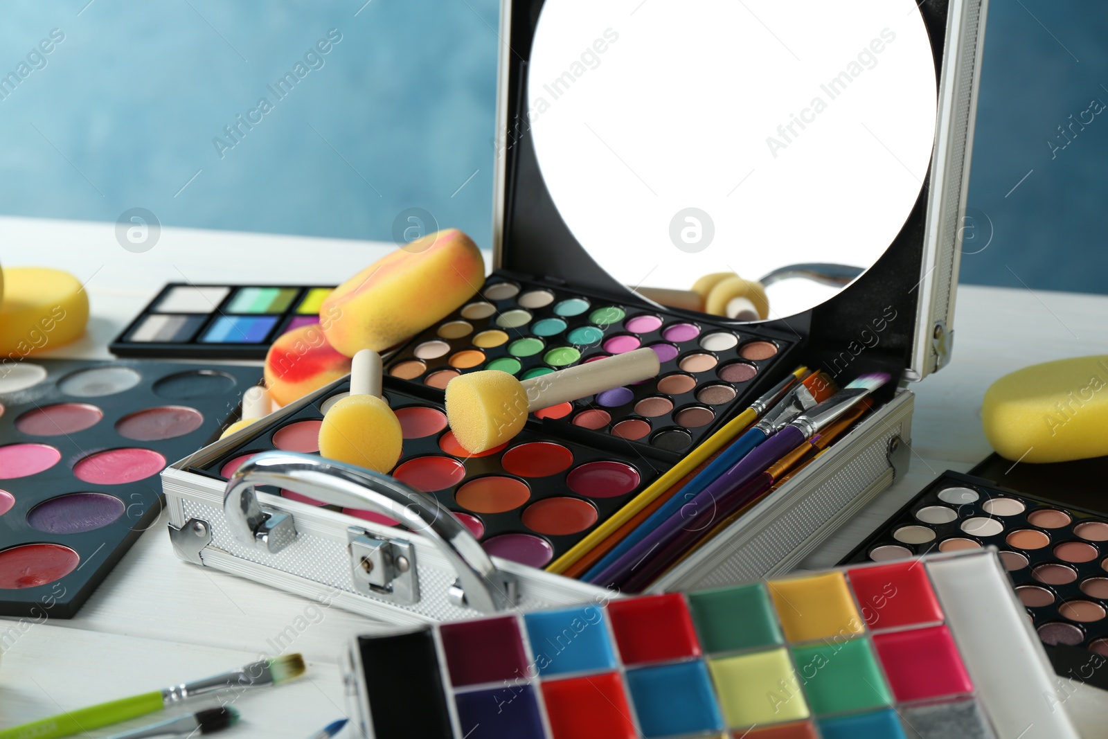 Photo of Face paints, tools and makeup products on white wooden table, closeup