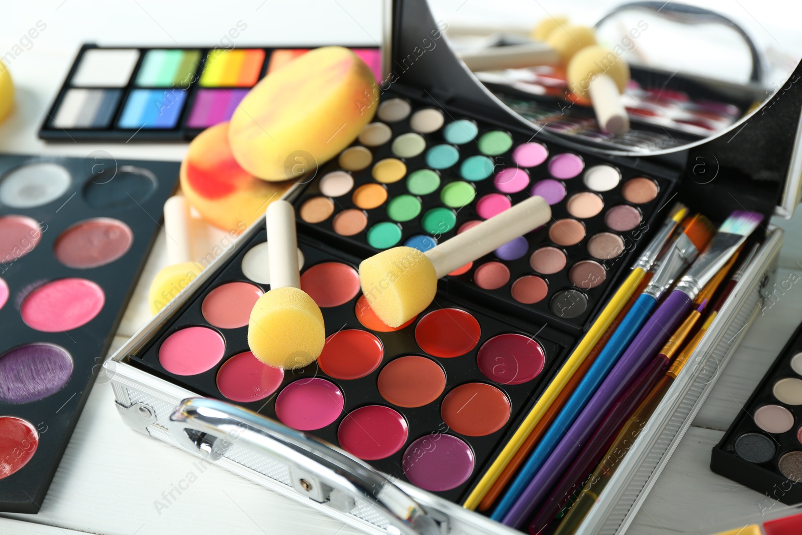 Photo of Face paints, tools and makeup products on white wooden background, closeup