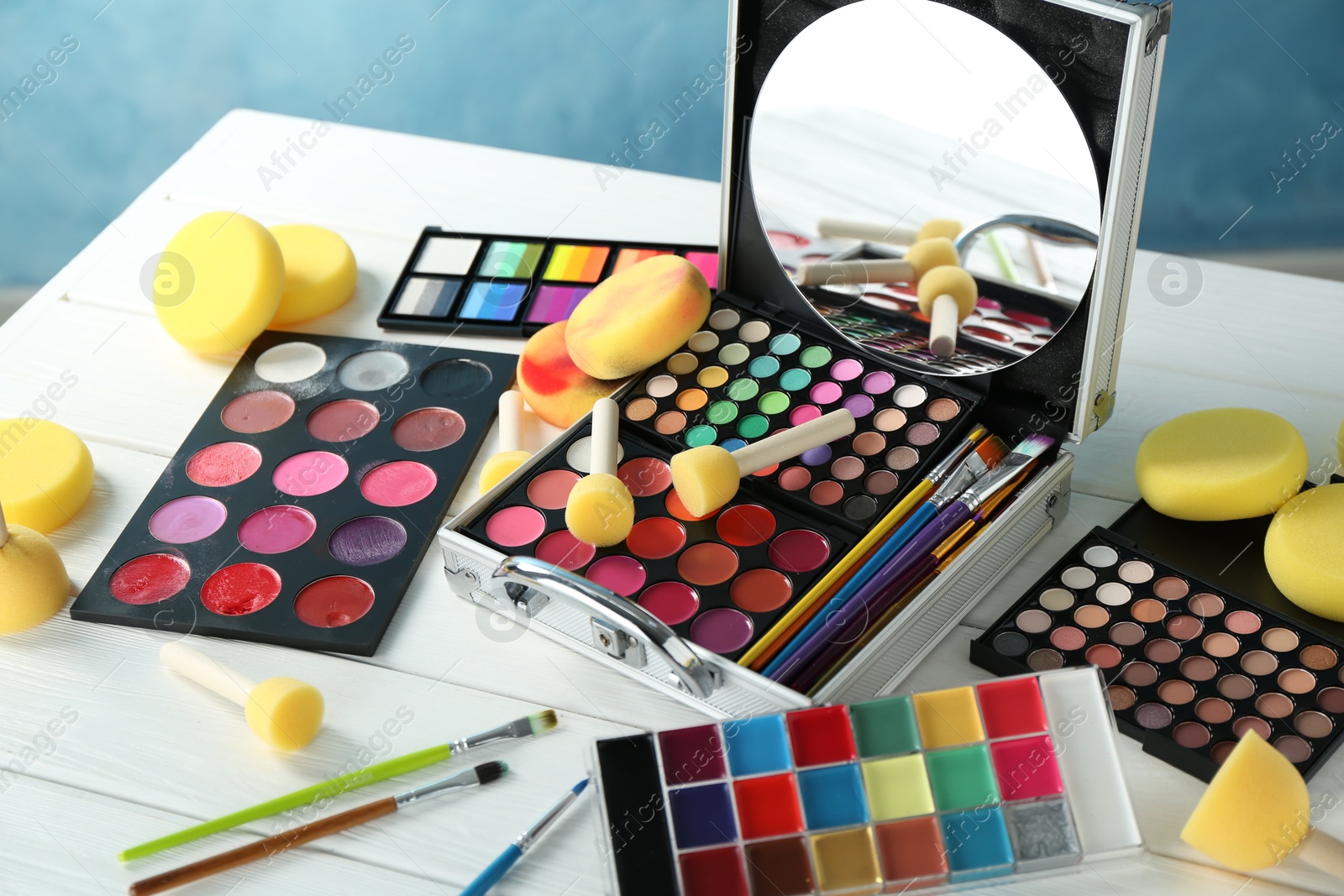 Photo of Face paints, tools and makeup products on white wooden table