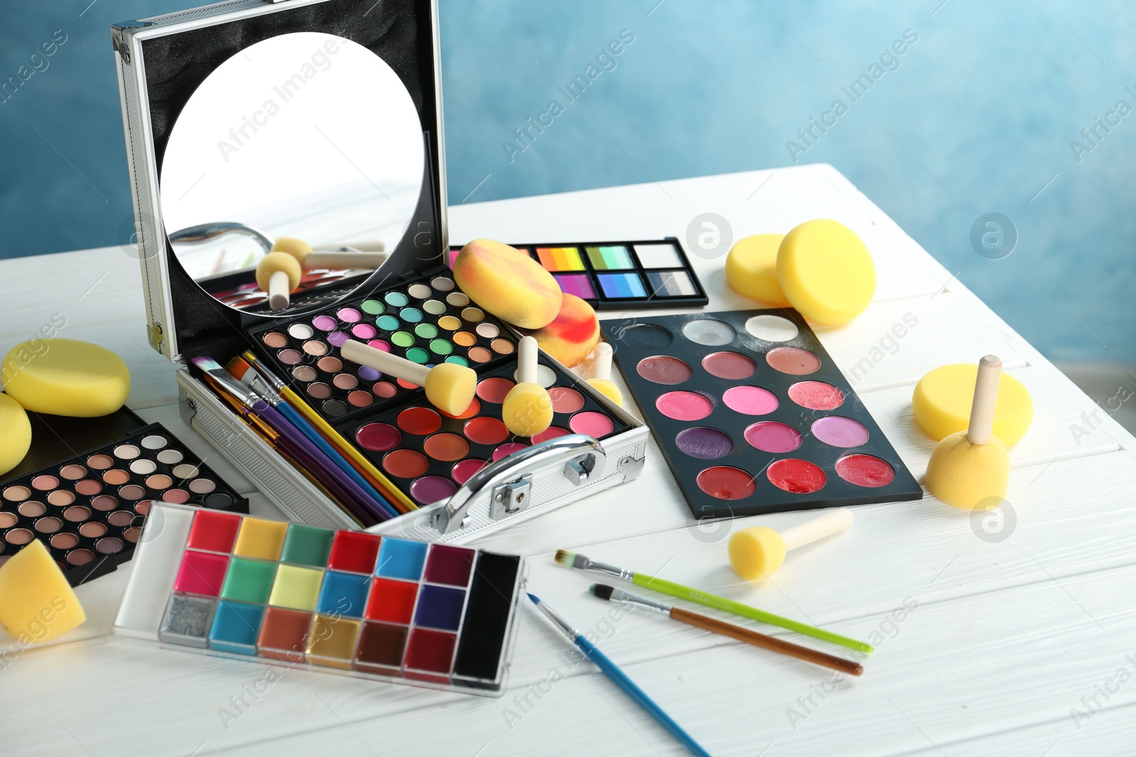 Photo of Face paints, tools and makeup products on white wooden table