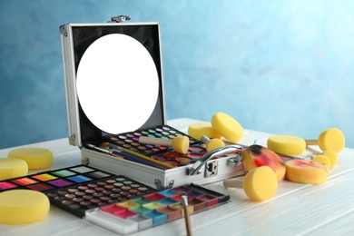 Photo of Face paints, tools and makeup products on white wooden table