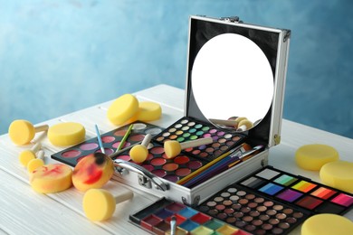 Photo of Face paints, tools and makeup products on white wooden table