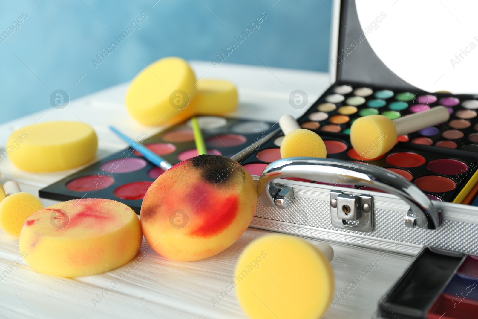 Photo of Face paints, tools and makeup products on white wooden background, closeup