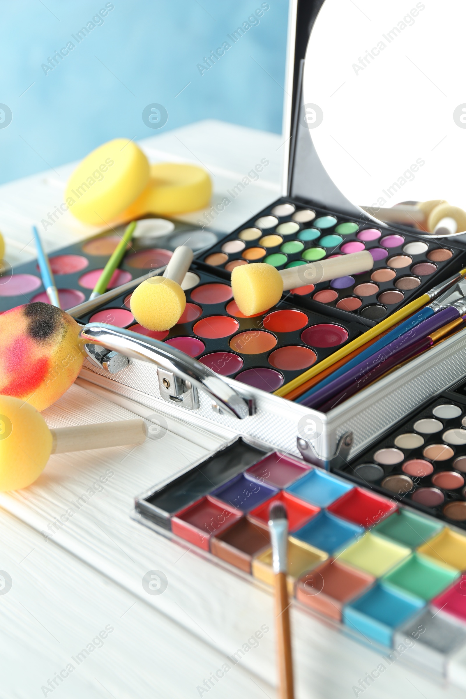 Photo of Face paints, tools and makeup products on white wooden background, closeup