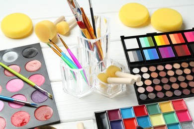 Photo of Face paints, tools and makeup products on white wooden background, closeup