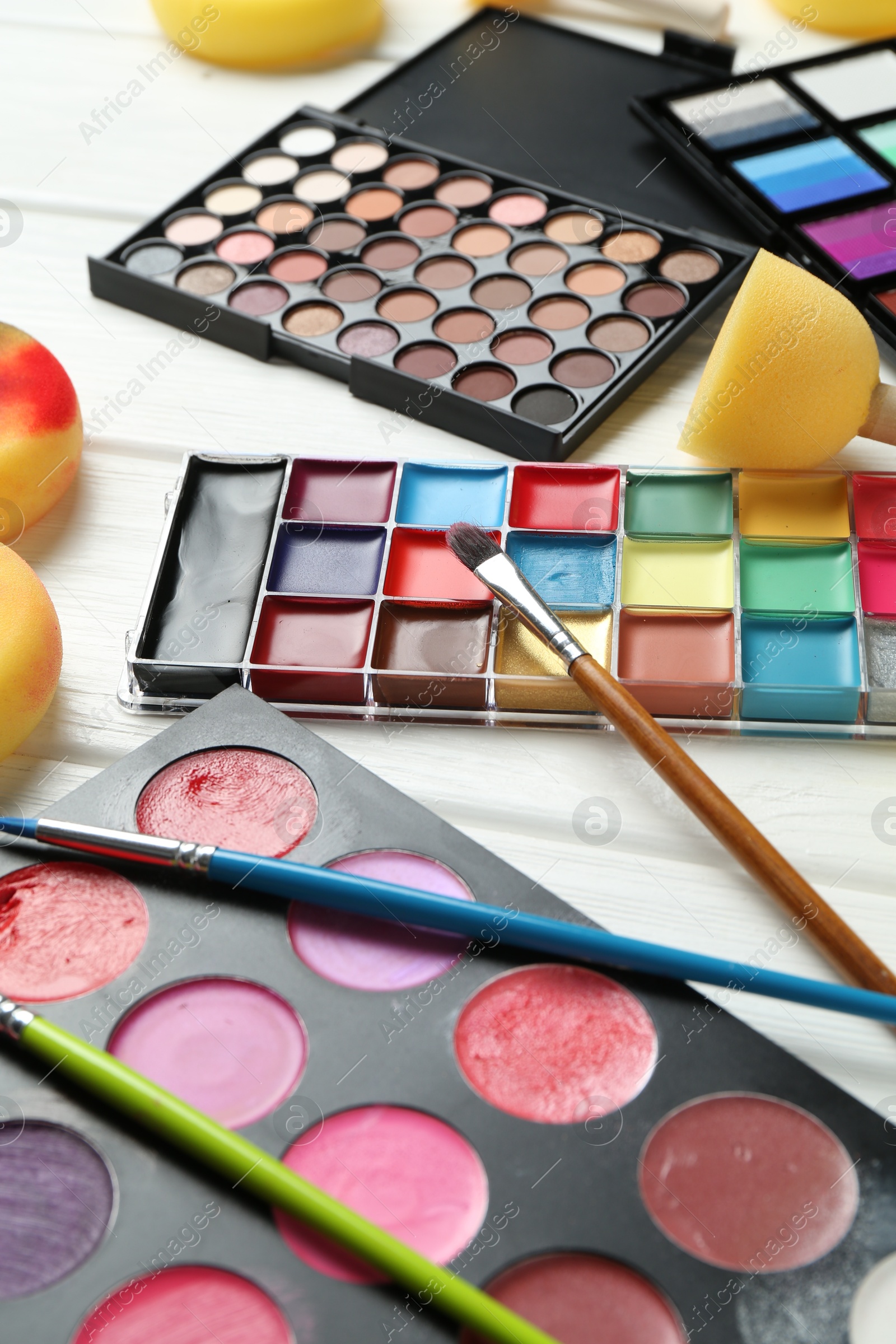 Photo of Face paints, tools and makeup products on white wooden background, closeup