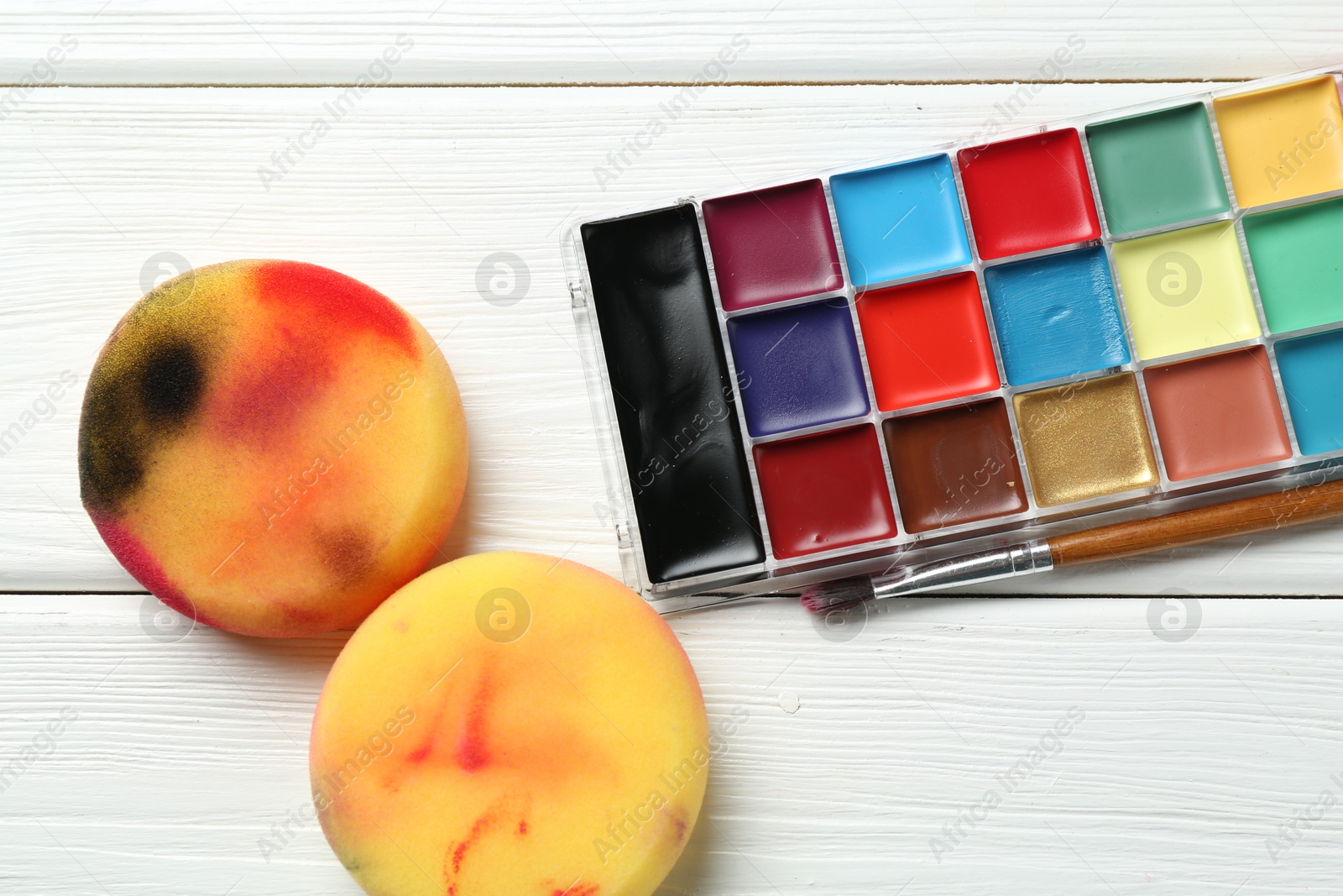 Photo of Face paints and sponges on white wooden table, closeup