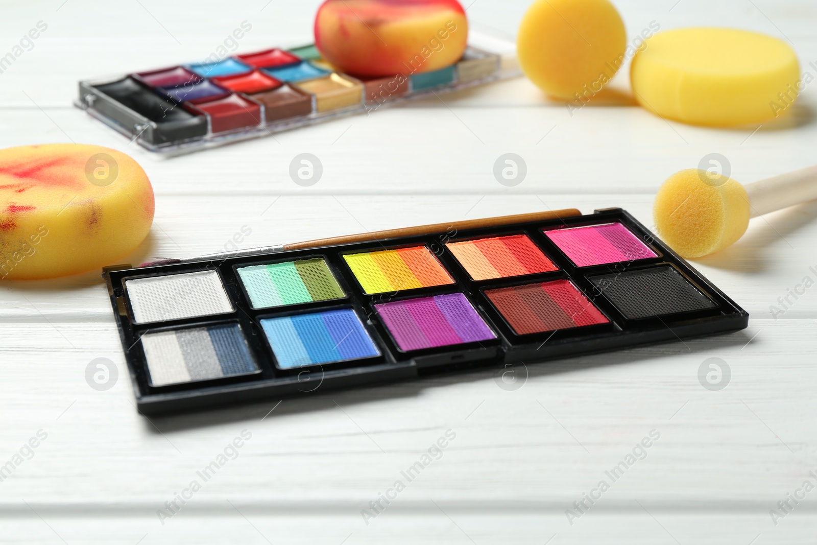 Photo of Face paints and tools on white wooden background, closeup