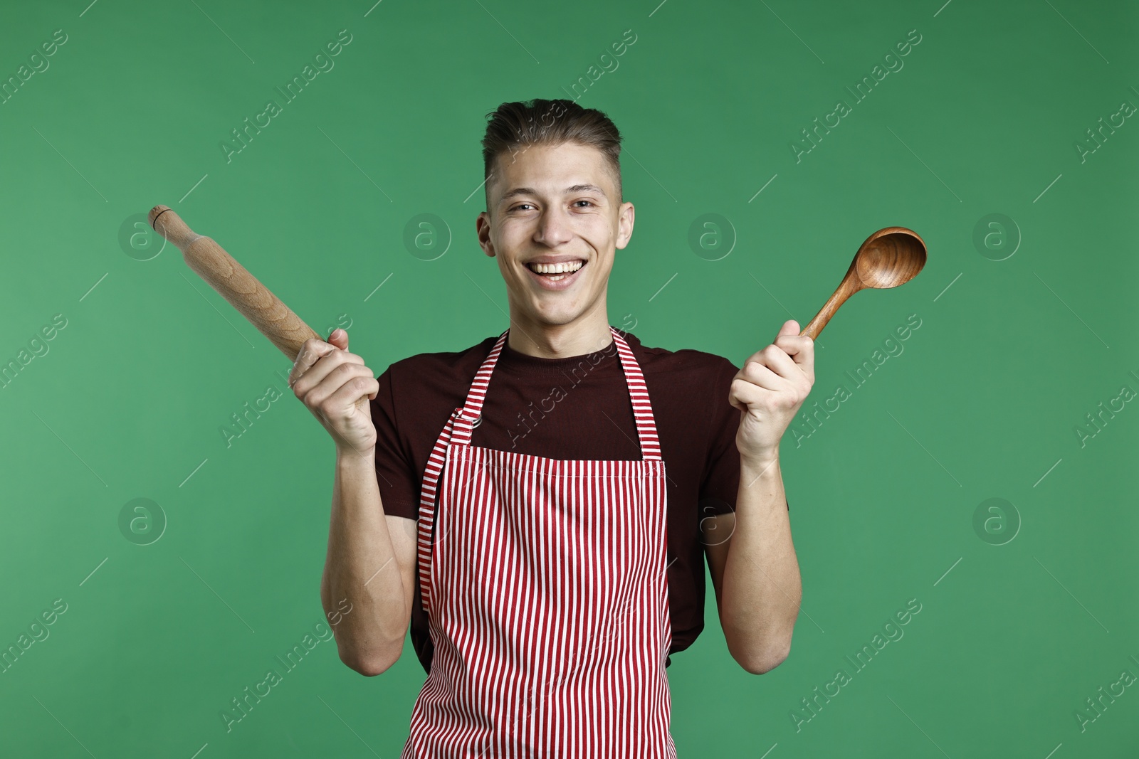 Photo of Happy man with rolling pin and spoon on green background