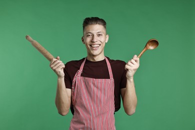 Photo of Happy man with rolling pin and spoon on green background