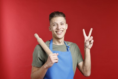 Photo of Happy man with rolling pin showing peace sign on red background