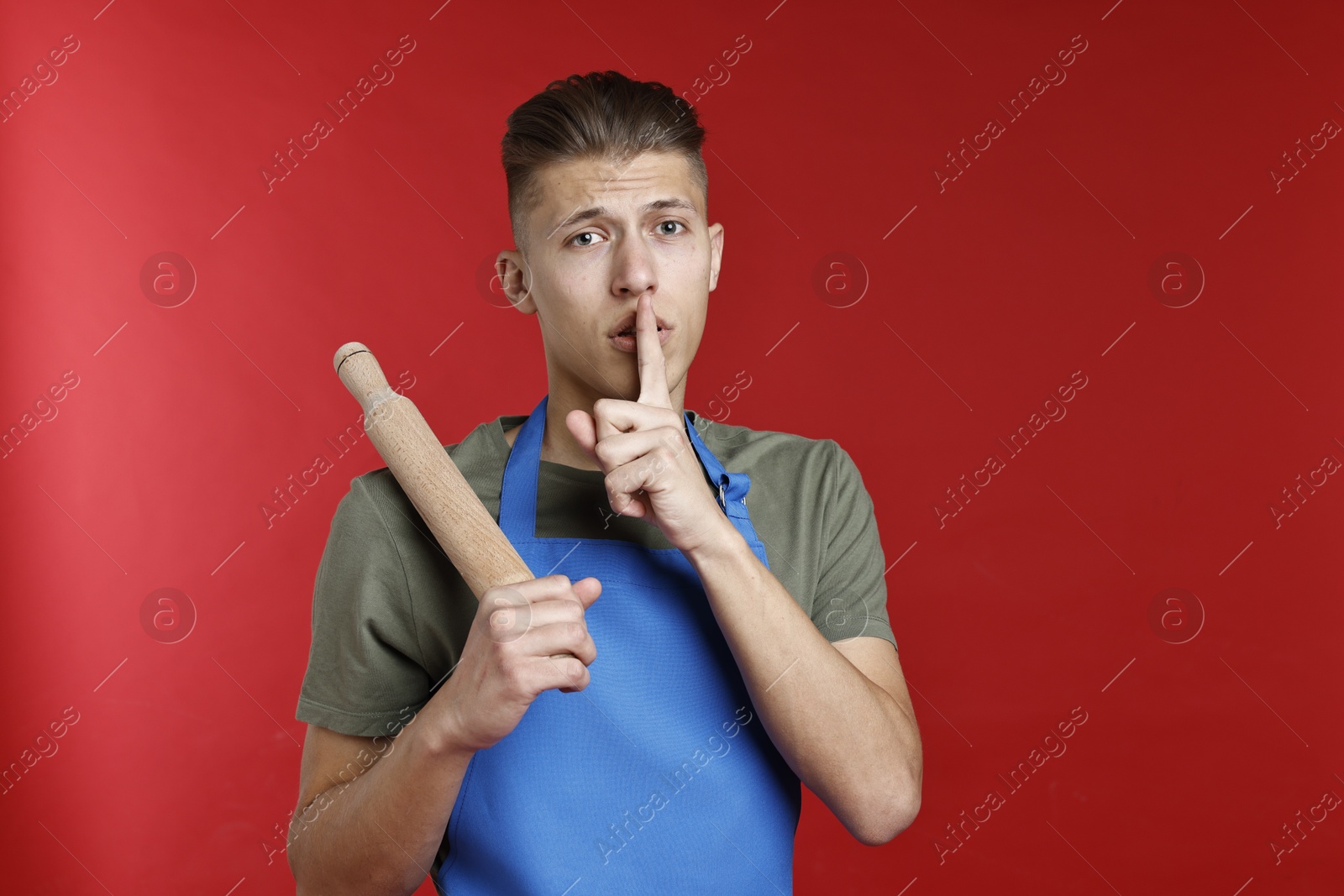 Photo of Man with rolling pin making hush gesture on red background