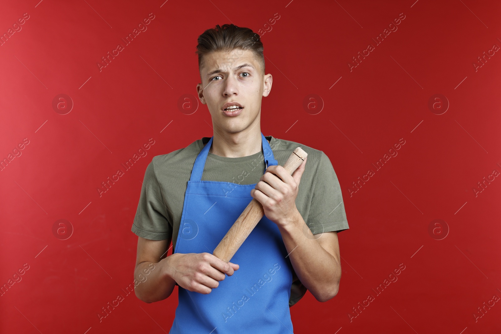 Photo of Confused man with rolling pin on red background