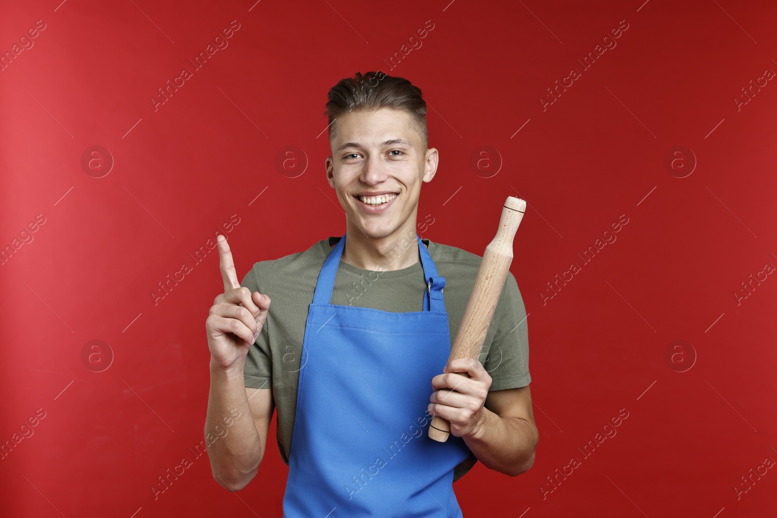 Photo of Happy man with rolling pin pointing at something on red background