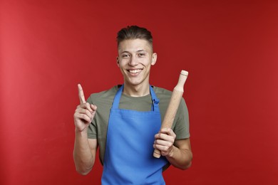 Photo of Happy man with rolling pin pointing at something on red background