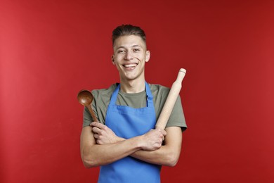 Photo of Happy man with rolling pin and spoon on red background