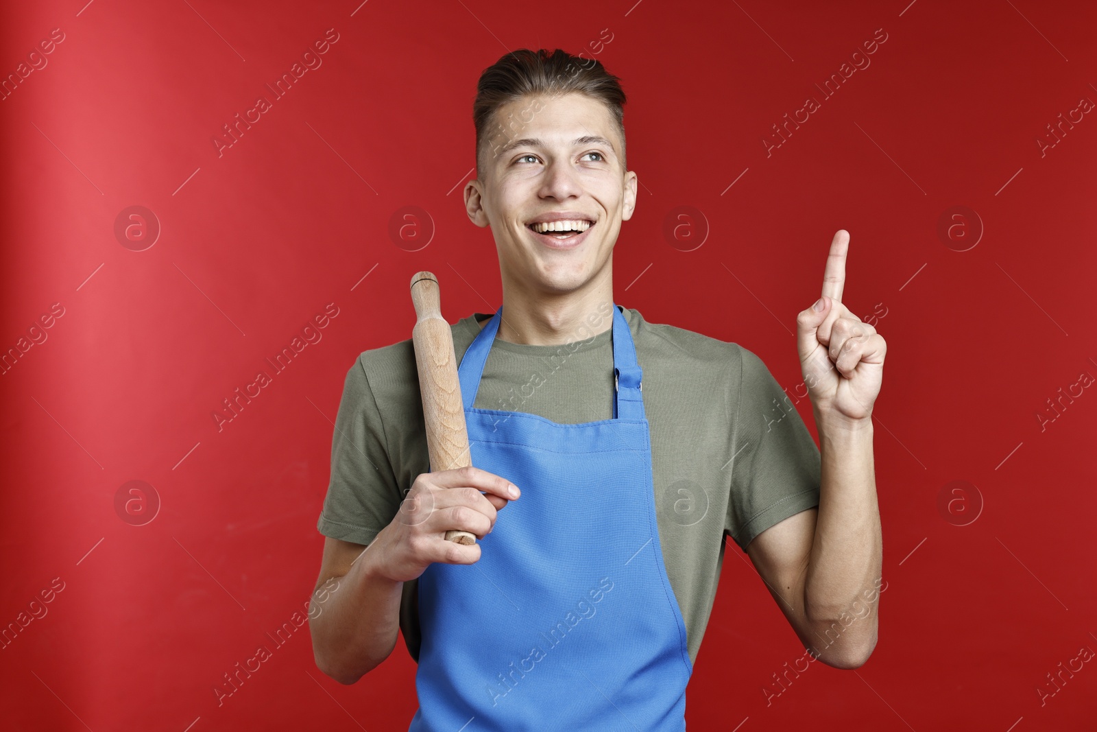 Photo of Happy man with rolling pin pointing at something on red background