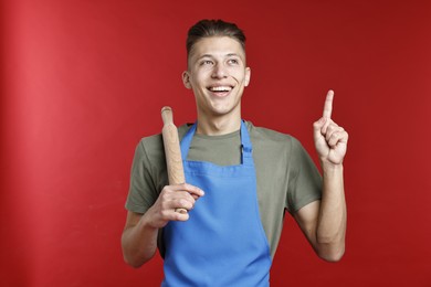 Photo of Happy man with rolling pin pointing at something on red background