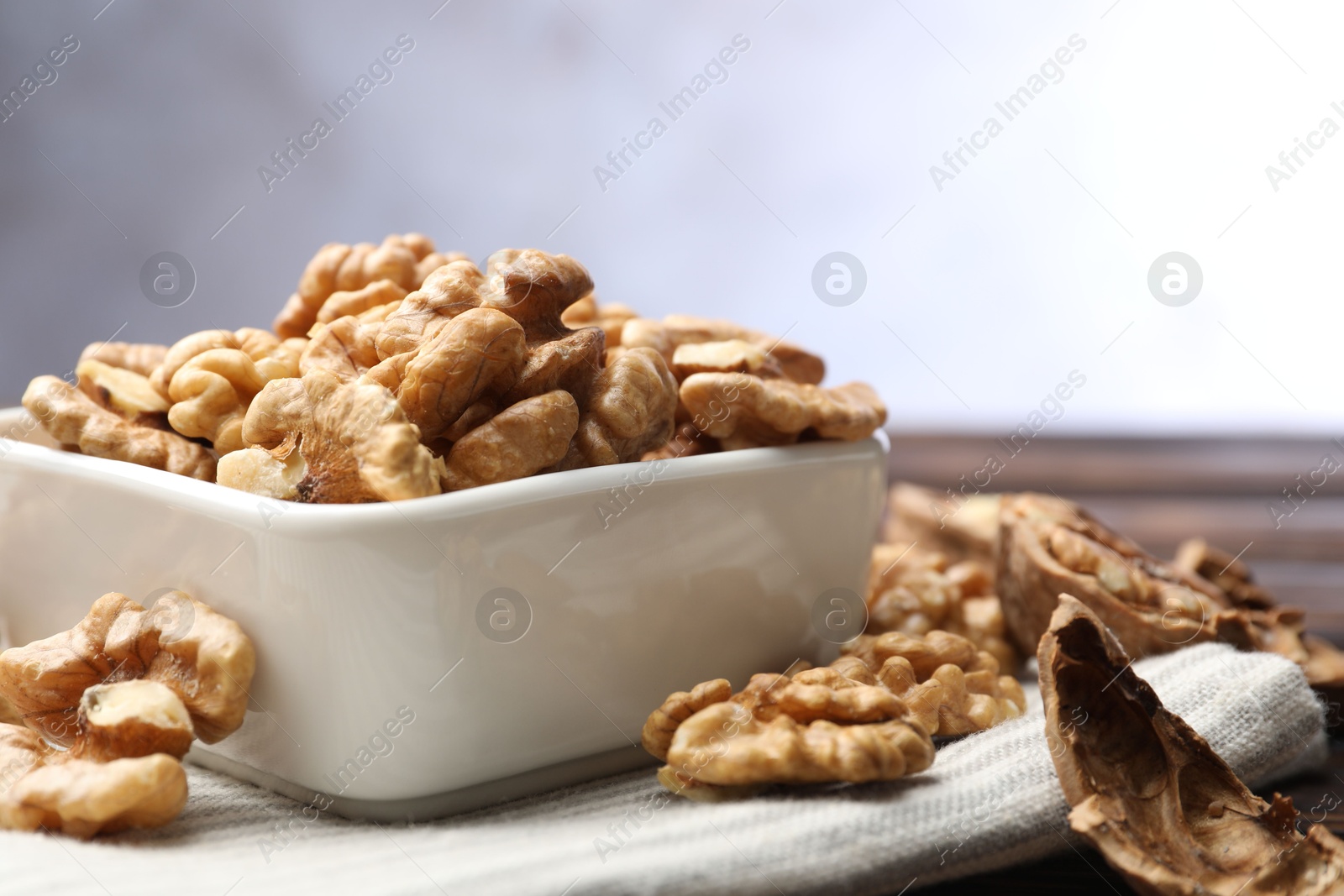 Photo of Peeled walnuts in bowl on table against light background, closeup. Space for text