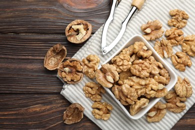 Photo of Peeled walnuts in bowl and nutcracker on wooden table, flat lay