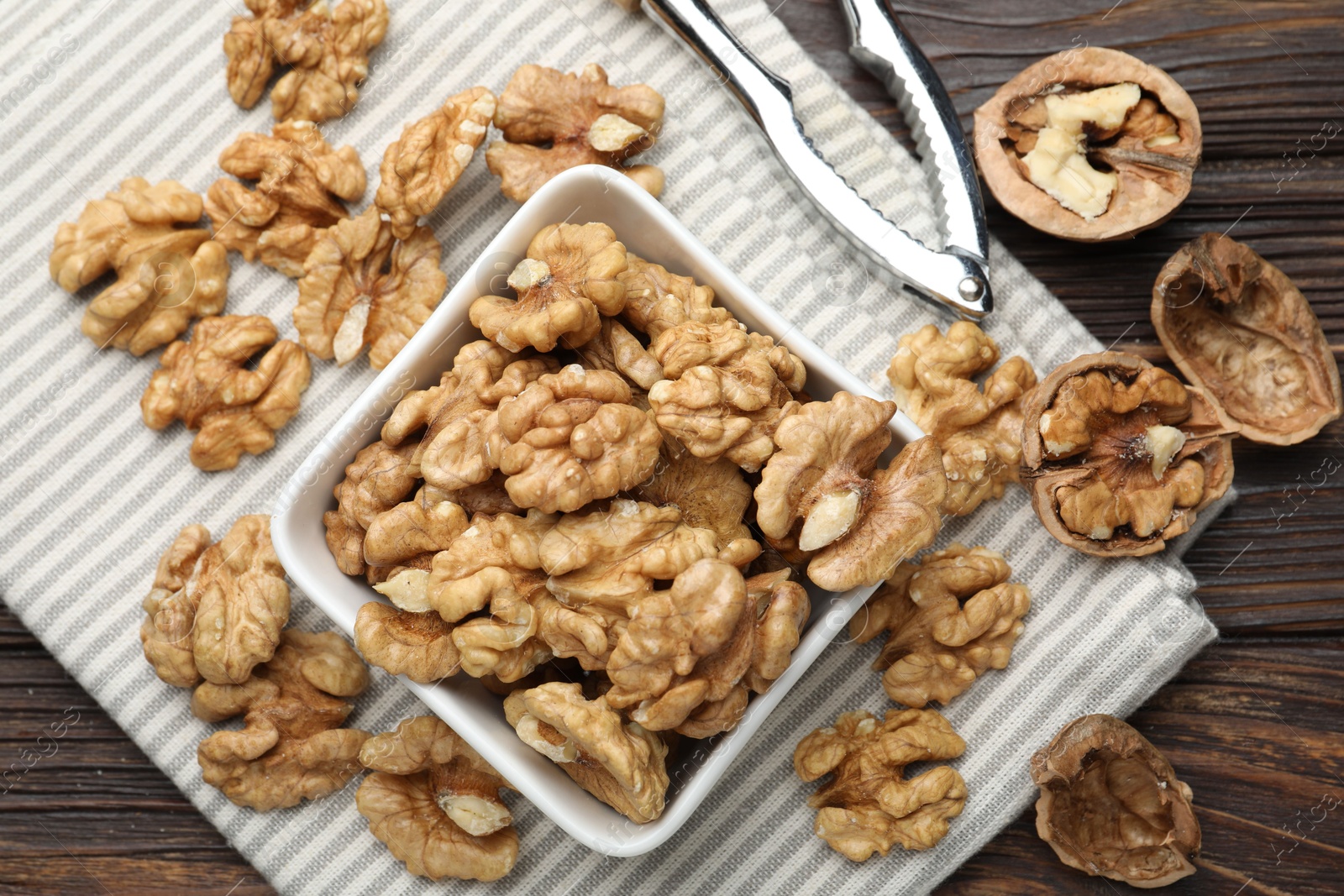 Photo of Peeled walnuts in bowl and nutcracker on wooden table, flat lay